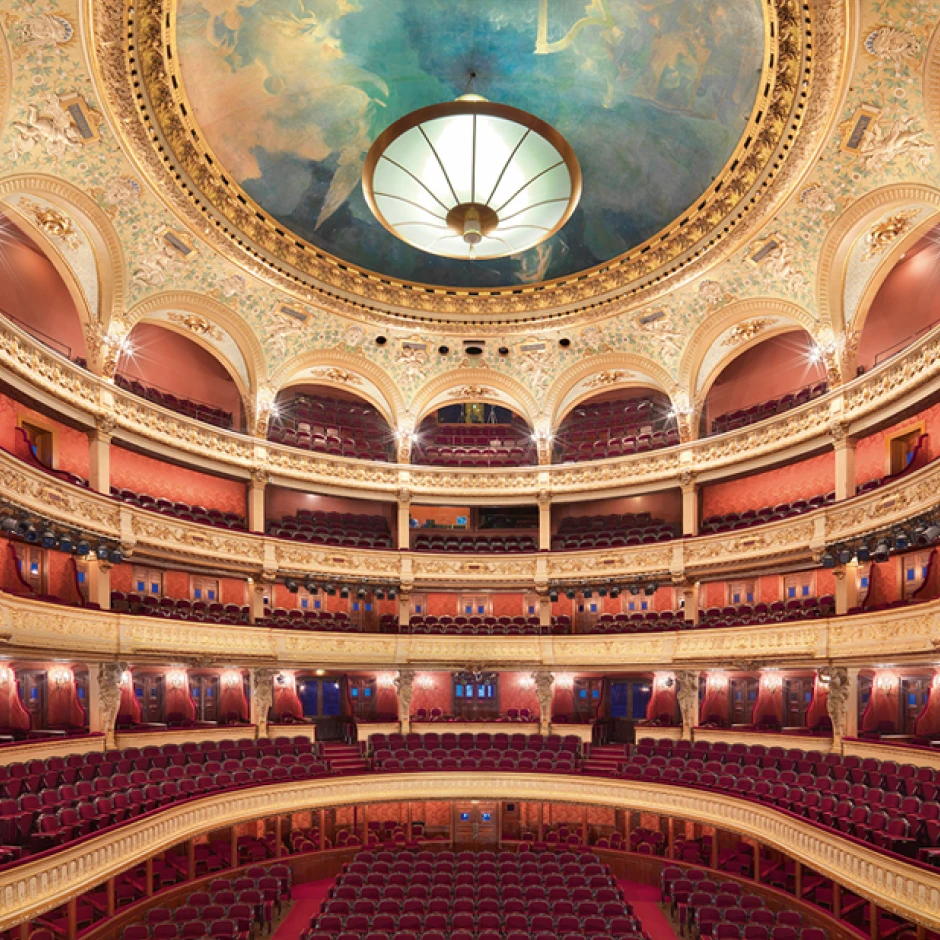 Photographie d’une salle d’opéra historique richement décorée avec balcons et fauteuils rouges.